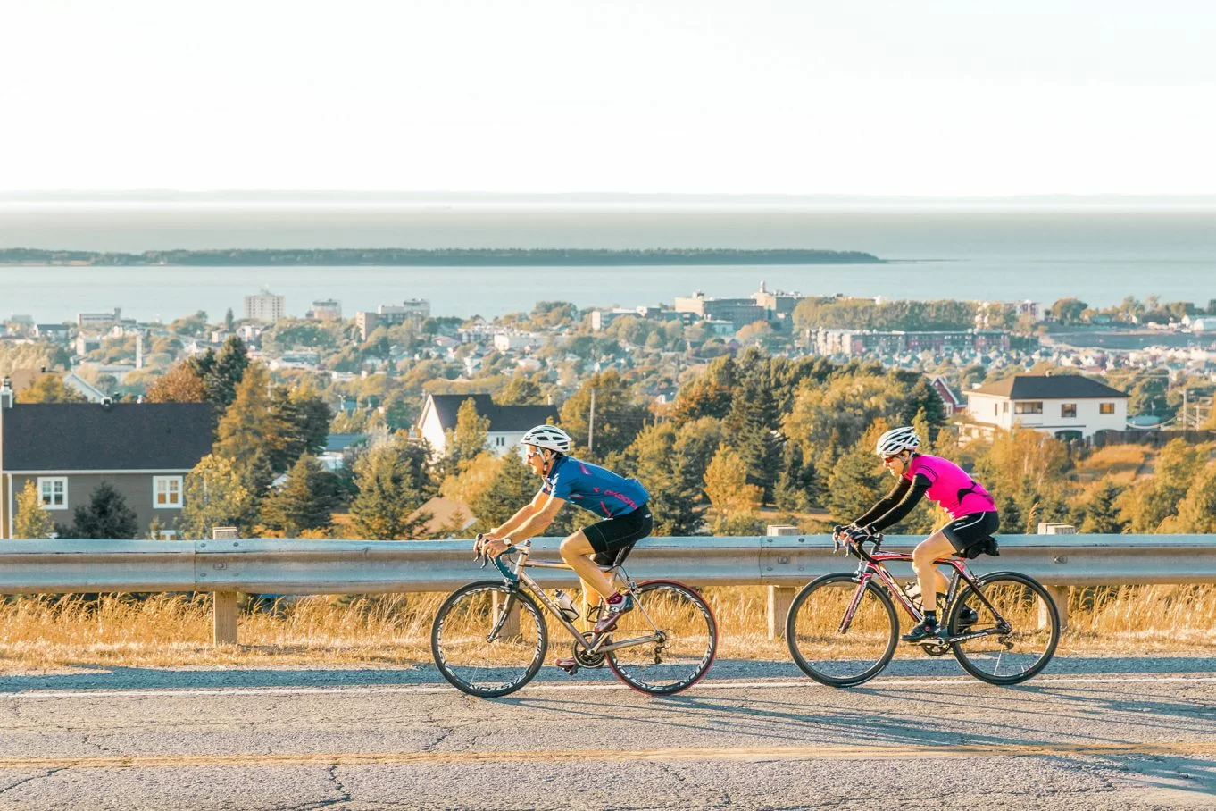 Cyclistes roulant près du fleuve avec vue sur une ville du Bas-Saint-Laurent.